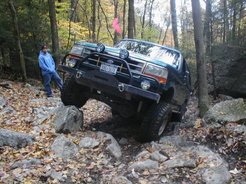 1979 Ford Bronco II - A green Ford Bronco tackles a challenging rocky terrain in a wooded area.