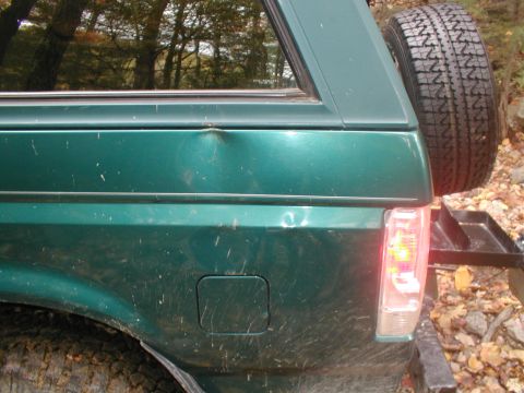 1979 Ford Bronco II - Rear view of a green SUV showing a dent on the quarter panel and a spare tire mounted externally.