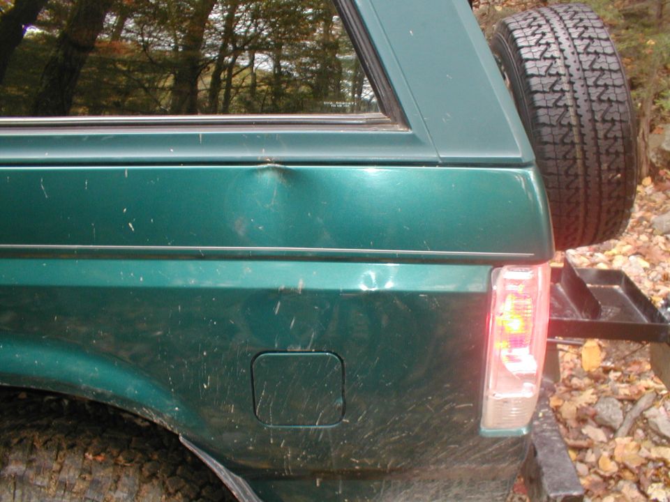 Green SUV rear quarter panel with dent, spare tire, and taillight