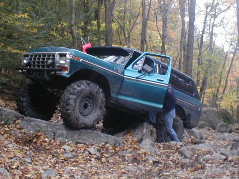 1979 Ford Bronco II - Teal off-road SUV with large tires navigating rocky terrain, appearing to be a 1979 Ford Bronco.