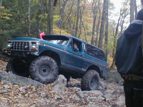 1979 Ford Bronco II - Ford Bronco tackling an off-road trail with large tires and a driver visible.