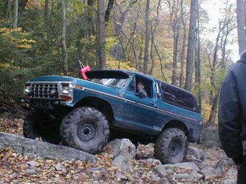 1979 Ford Bronco II - A teal Ford Bronco navigates a rocky trail in a forest setting during autumn.