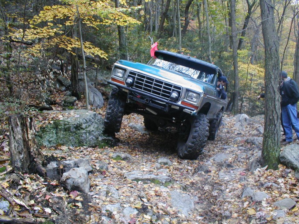 Teal Ford Bronco climbing over rocks on a wooded trail