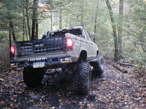 1979 Ford Bronco II - This heavily modified pickup truck, possibly a Ford Ranger, navigates a wooded trail with large off-road tires.