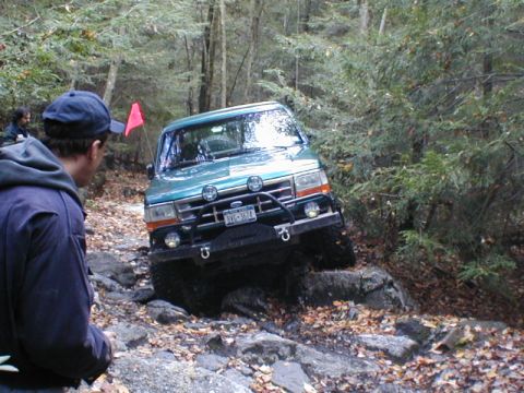 1979 Ford Bronco II - A green Ford Bronco is shown off-roading on a rocky, wooded path.