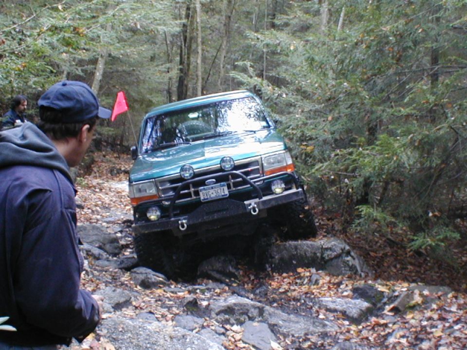 Green Ford Bronco navigating a rocky trail with a person watching