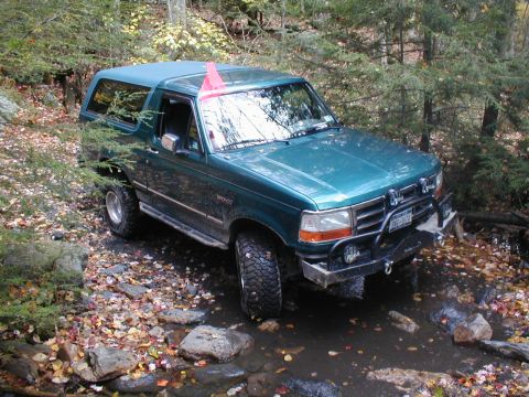 1979 Ford Bronco II - This green SUV navigates a rocky stream surrounded by trees and fallen leaves.