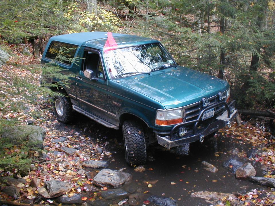 Green SUV with a pink flag on the roof driving through a rocky stream