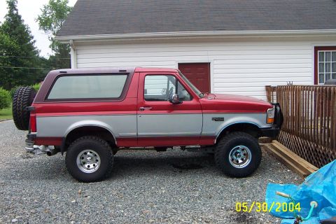 1996 Ford Bronco - Side view of a lifted red and silver Ford Bronco with a spare tire mounted externally.