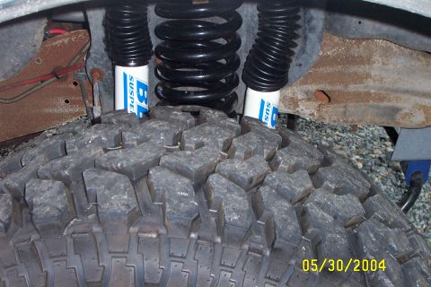 1996 Ford Bronco - This image shows a close-up view of a lifted suspension system, large tires and blue shock absorbers.