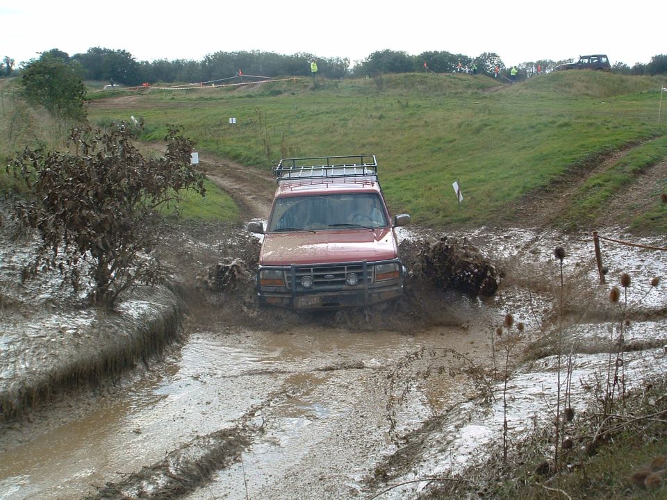 Red 1995 Ford Bronco driving through a mud pit on an off-road course