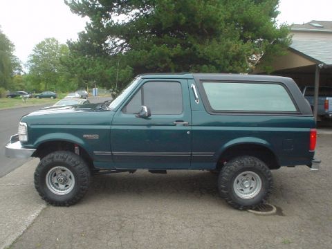 1993 Ford Bronco - Side profile of a lifted green 1993 Ford Bronco with a black hardtop and off-road tires.