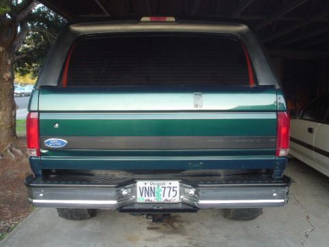 1993 Ford Bronco - The rear of a green Ford Bronco is visible, parked under a cover with a tree to the left.