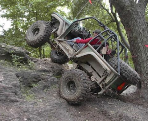 1992 Ford Bronco - An off-road buggy navigates a steep, rocky incline with one wheel lifted high off the ground.