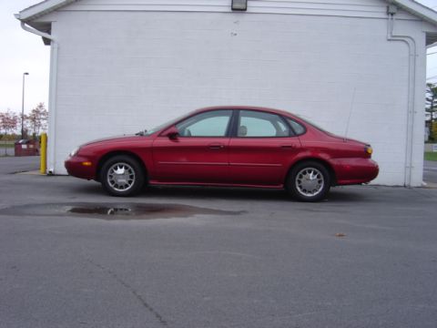 1998 Ford Taurus - A red 1998 Ford Taurus is parked on asphalt in front of a white building.