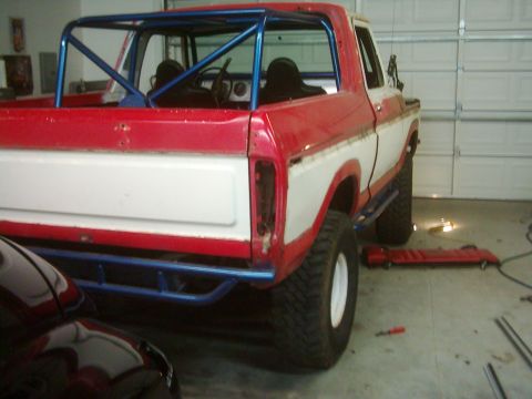 1978 Ford Bronco - This red and white 1978 Ford Bronco features a prominent blue roll cage and off-road tires, viewed from the rear.