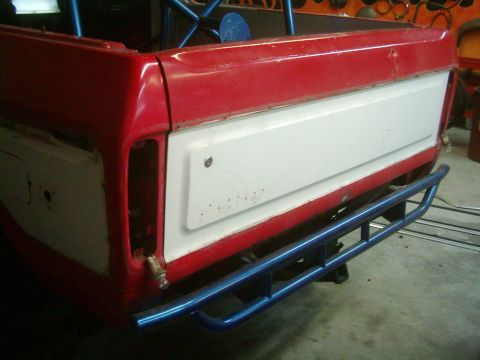 1978 Ford Bronco - The rear of a red and white pickup truck bed is shown, a blue bumper and roll cage structure.