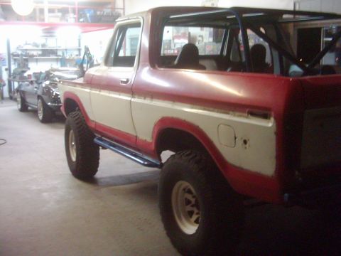 1978 Ford Bronco - This red and white 1978 Ford Bronco features a roll cage and is parked next to another vehicle in a garage.