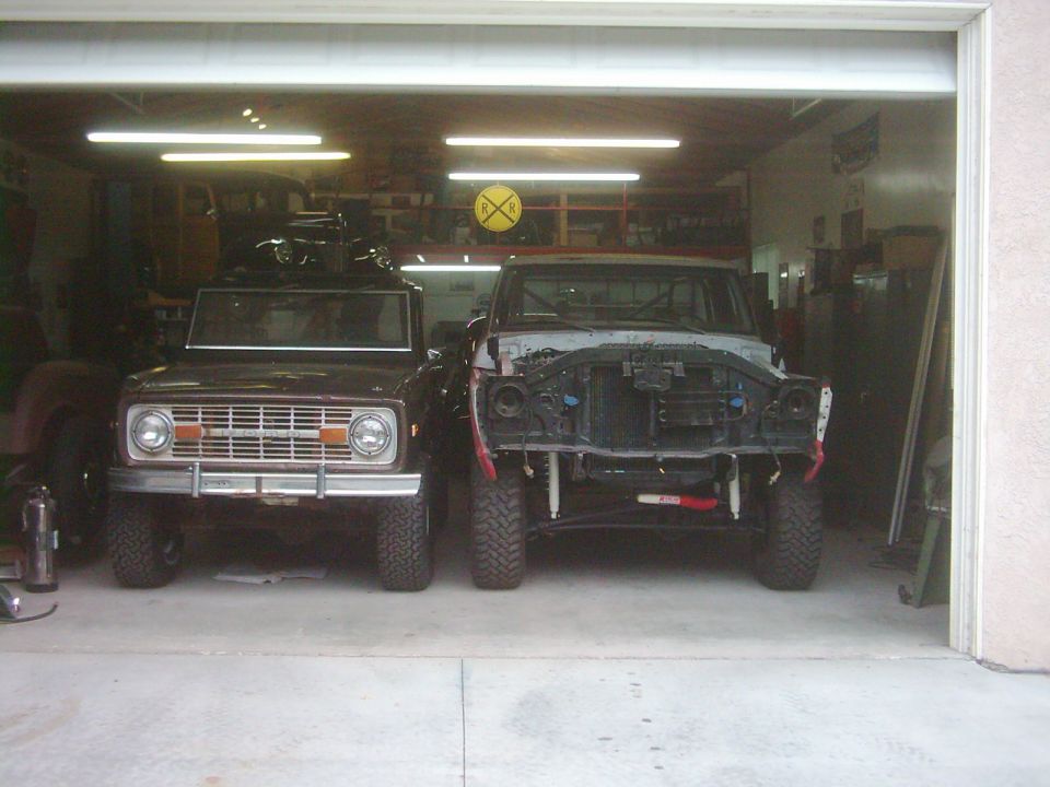 Brown 1978 Ford Bronco front view next to a disassembled truck in a garage