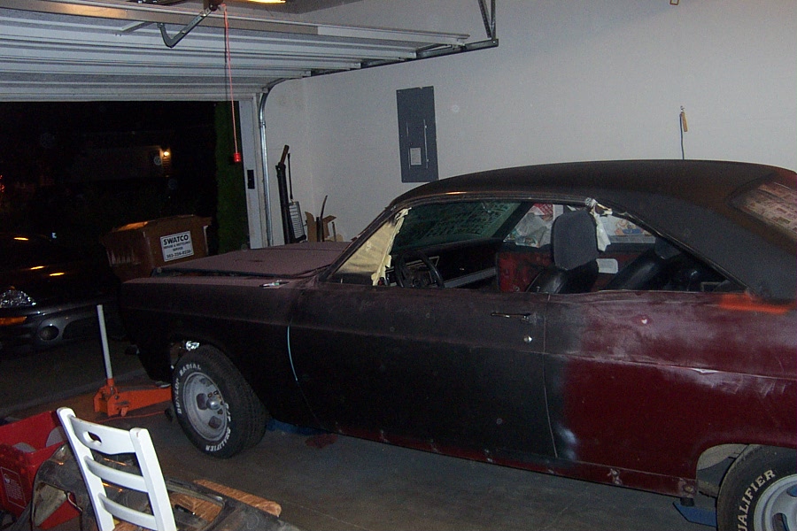 Side view of dark burgundy 2-door coupe on jack stand in a garage