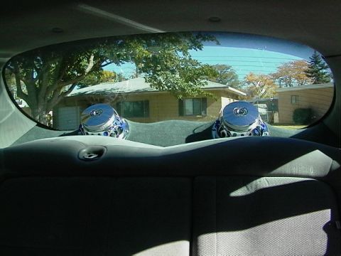 1999 Ford Taurus - View from inside a car's back seat shows two aftermarket speakers and a residential scene through the rear window.