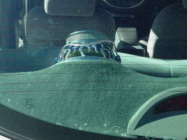 Aftermarket car speaker mounted on a rear deck, seen through a rear window