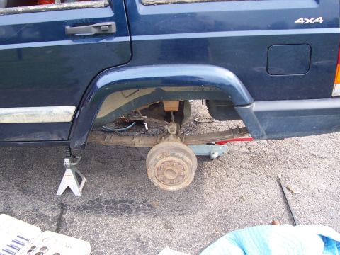 2000 Jeep Cherokee - The rear axle and leaf springs of a blue Jeep Cherokee are visible as the vehicle is lifted on jack stands.