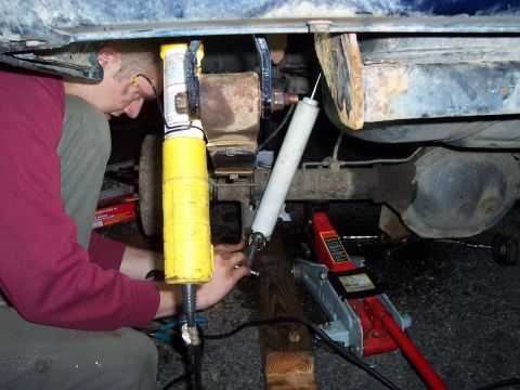 2000 Jeep Cherokee - A person works on the undercarriage of a vehicle, adjusting suspension components with a jack and tools.