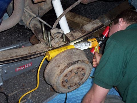 2000 Jeep Cherokee - Mechanic works on the rear axle of a vehicle, with a jack and tools visible.