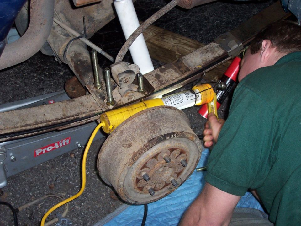 Man using a tool on a vehicle's rear axle assembly, supported by a Pro-Lift jack