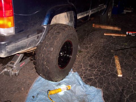 2000 Jeep Cherokee - A Jeep Cherokee is being lifted by a jack, with a large off-road tire visible.