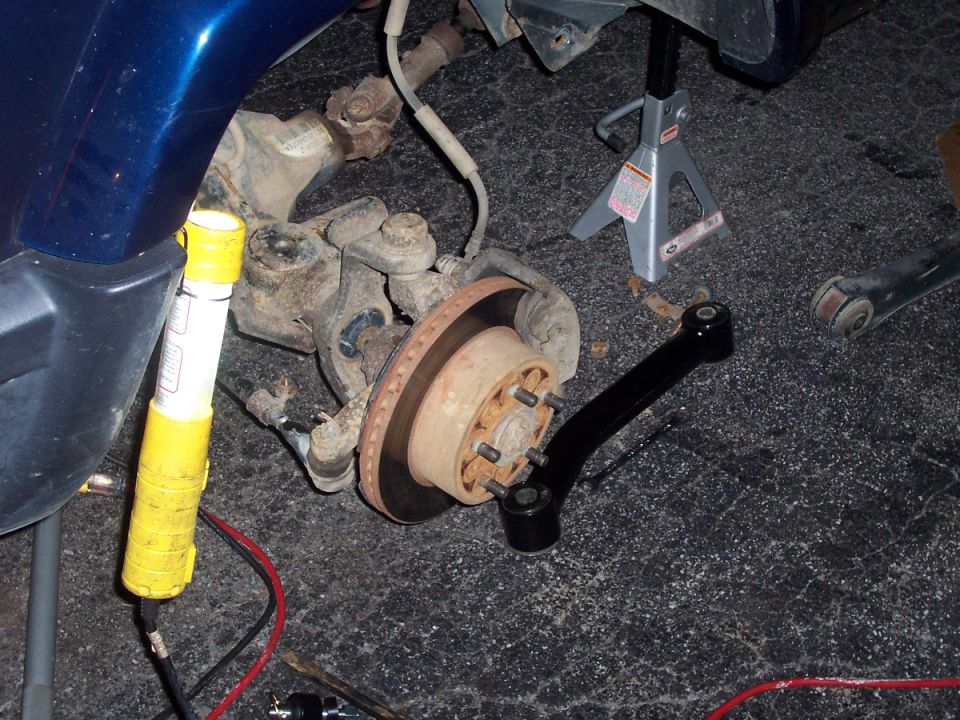 Front hub and rotor exposed during suspension work with new black control arm on floor