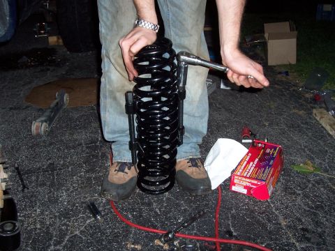 2000 Jeep Cherokee - Using a spring compressor tool on a coil spring, with a parts box in the background.