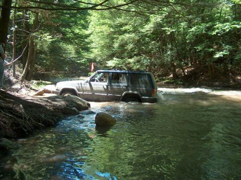 2000 Jeep Cherokee - A Jeep Cherokee navigates a rocky riverbed surrounded by dense trees.