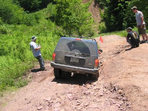 2000 Jeep Cherokee navigating a rough dirt trail with people watching