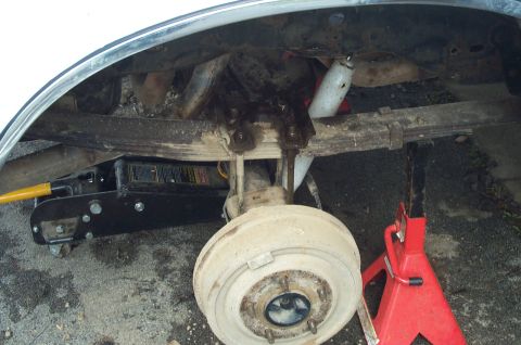 1988 Ford Bronco - The rear suspension and axle assembly of a vehicle are shown, with a floor jack and a red jack stand providing support.
