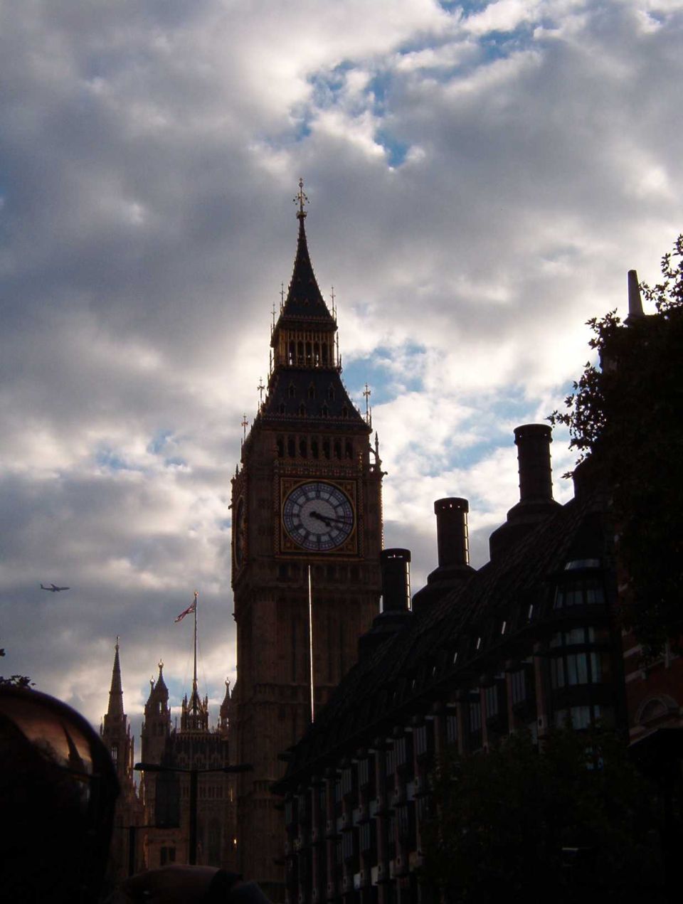 Big Ben clock tower backlit against dramatic clouds with chimneys in the foreground
