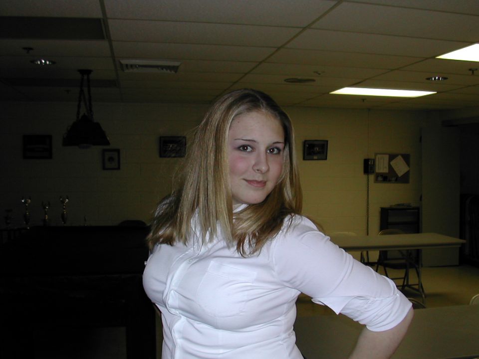 Young woman with blond hair in a white top posing in a dim paneled basement room