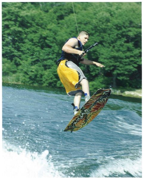 1993 Ford Bronco - A wakeboarder performs a trick while being pulled across the water, with a lush green forest visible behind them.
