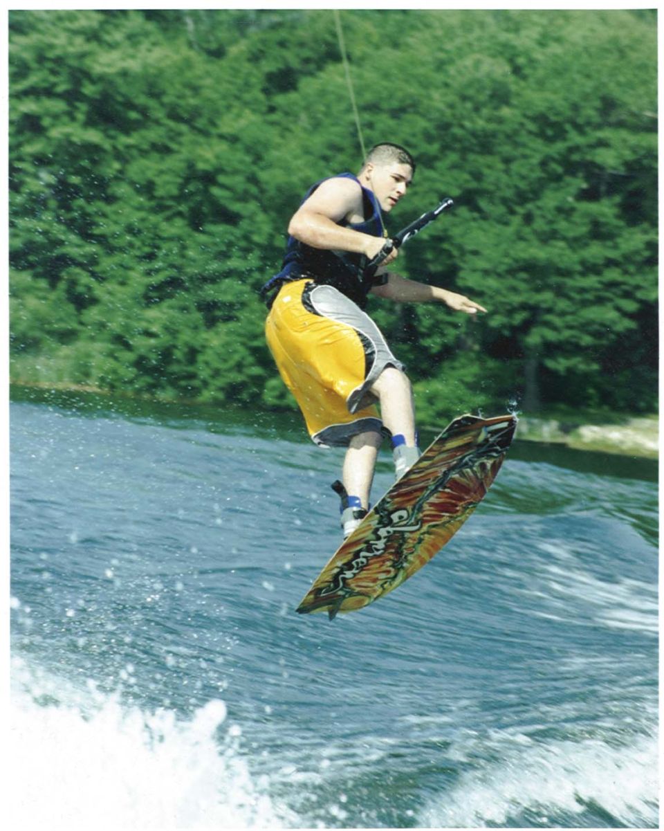 Wakeboarder mid-air over water with trees in background