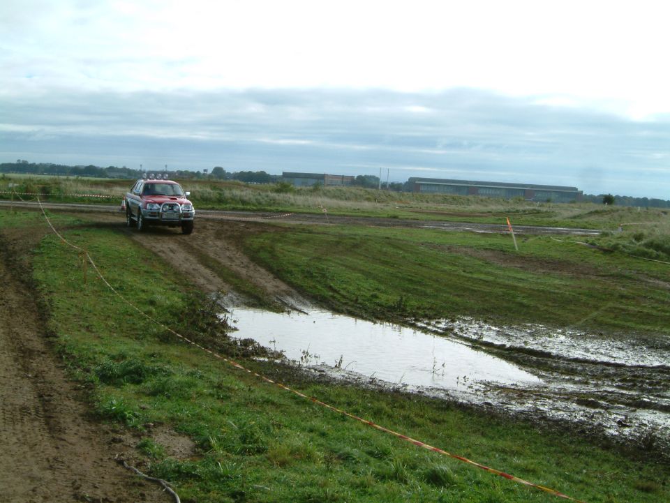 Red off-road SUV driving through muddy terrain with puddles
