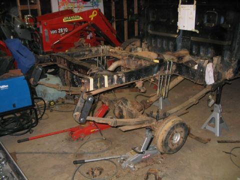 1986 Ford F-150 - The chassis of a truck is disassembled and supported by jack stands in a garage setting.