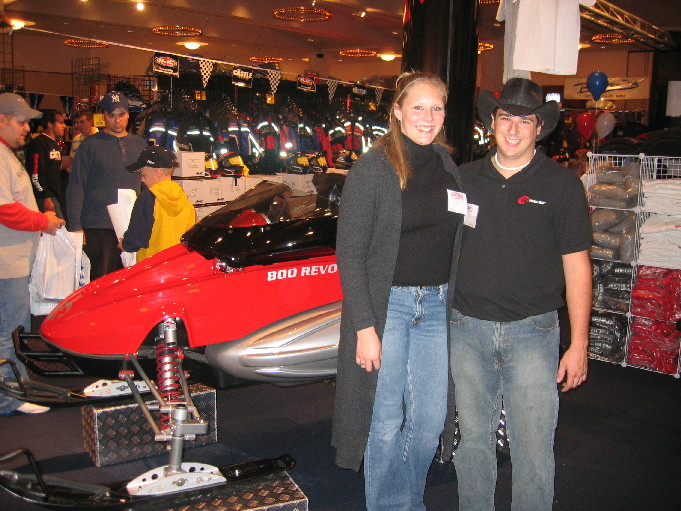 People stand next to a red snowmobile with '800 REVO' on its side