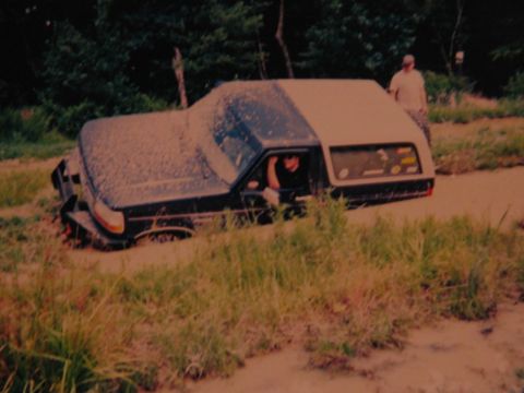1995 Ford Bronco - A Ford Bronco is stuck in the mud with a person inside and another person standing nearby.