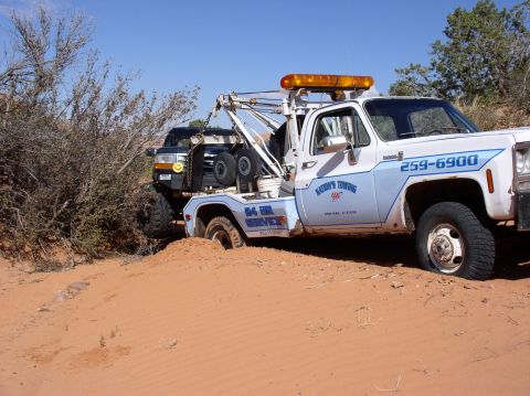 1993 Ford Bronco - A tow truck is working to free a black SUV that is stuck in the sand dunes.