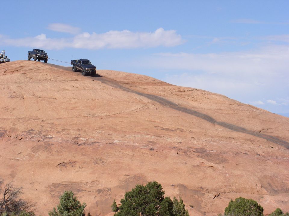 Two trucks on a rocky incline, one towing the other