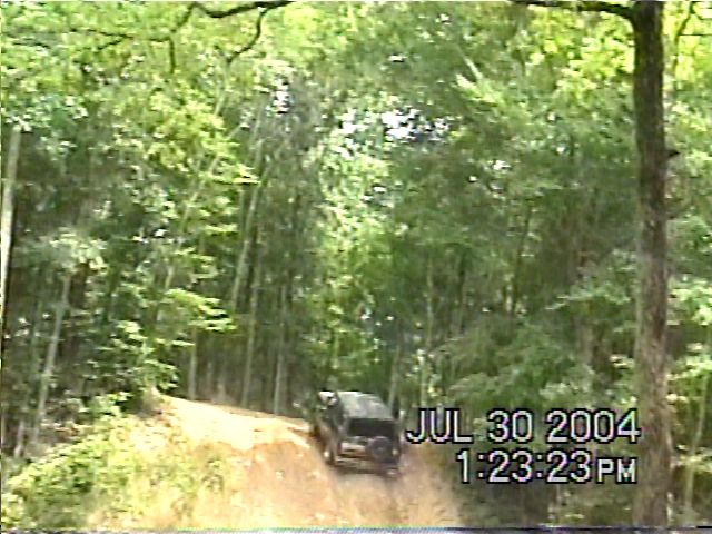 1988 Ford Bronco driving up a dirt hill in a wooded area. Date stamp shows JUL 30 2004 1:23:23 PM