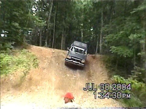 1988 Ford Bronco - A dark SUV navigates a steep dirt incline surrounded by dense forest.