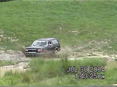 1988 Ford Bronco - A 1988 Ford Bronco navigates a muddy off-road course, kicking up water and dirt.