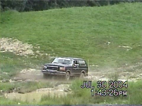1988 Ford Bronco - A dark SUV navigates a muddy track on a grassy hillside, with a timestamp indicating July 30, 2004.